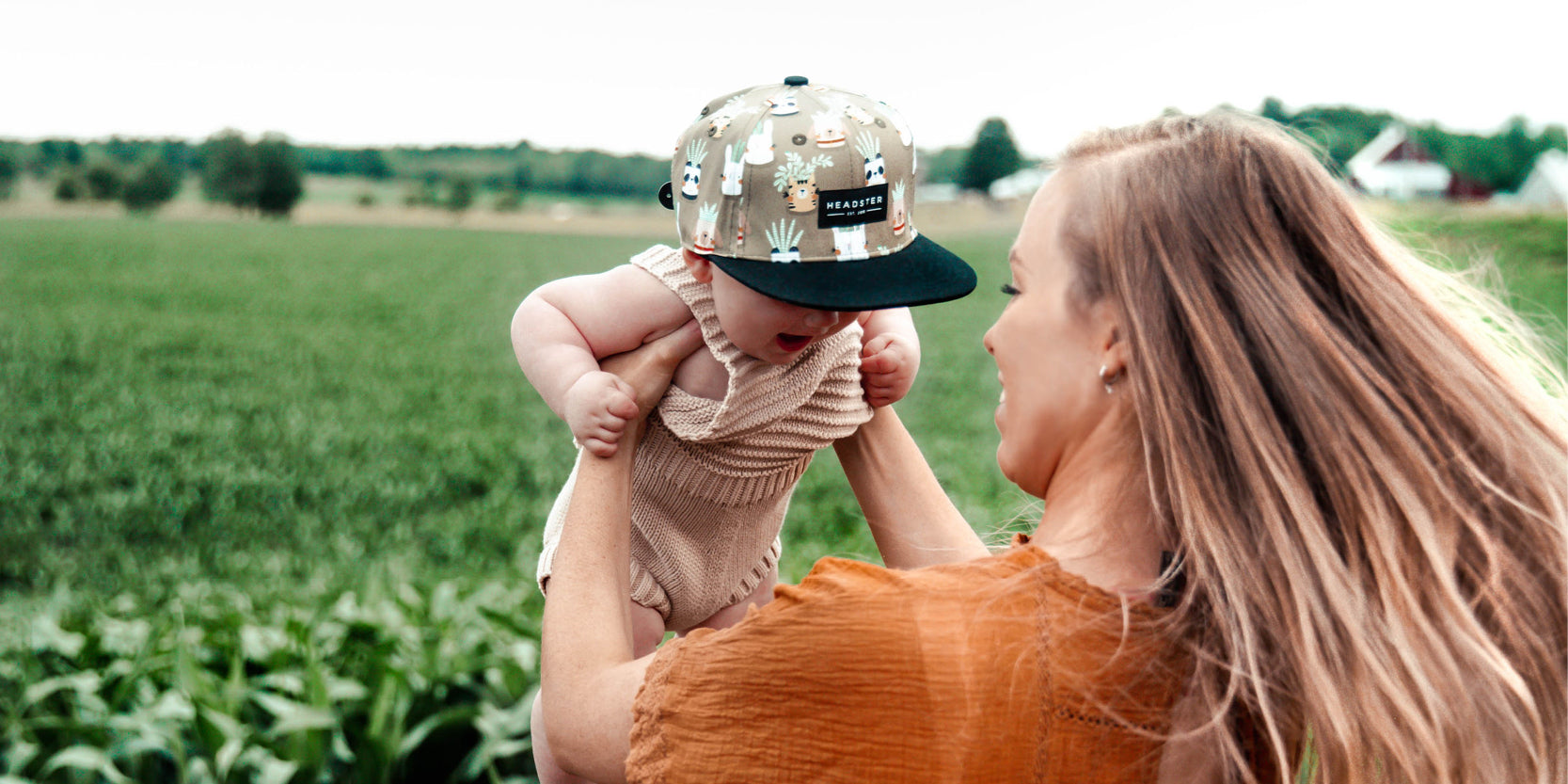 Une maman dans un champs vert avec un bébé avec une casquette Headster