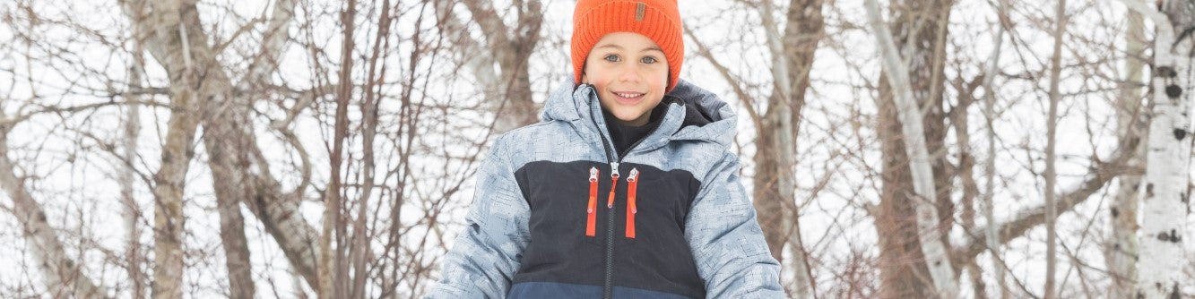un enfant garçon avec une tuque orange et un manteau d'hiver de la marque peluche et tartine