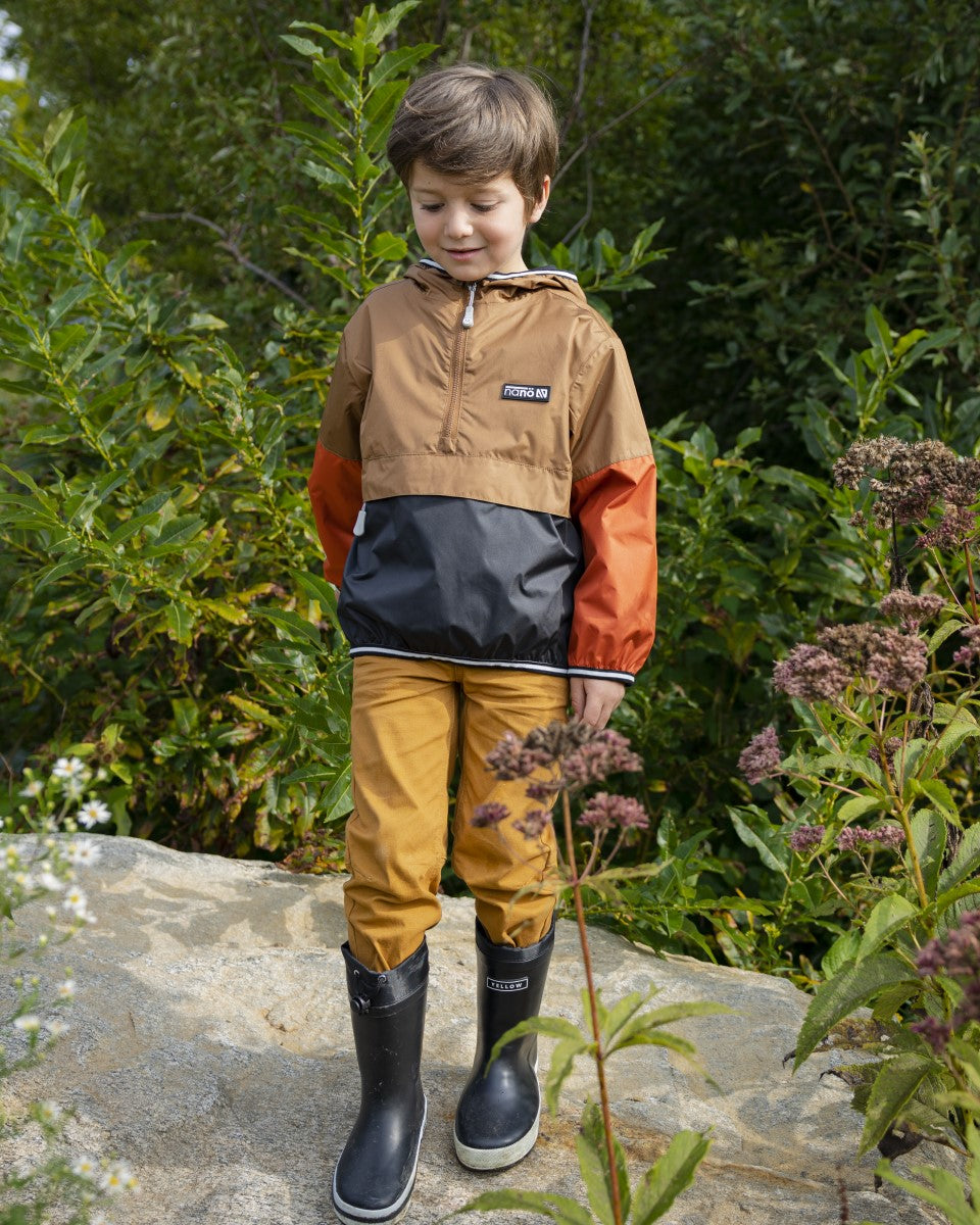 Jeune garçon prend une photo habillé avec un coupe-vent et des bottes de pluie