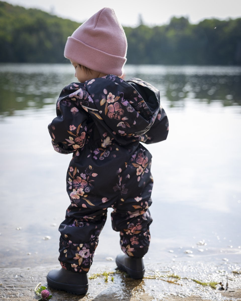 Bébé fille sur le bord de l'eau dans un habit de pluie rose et noir